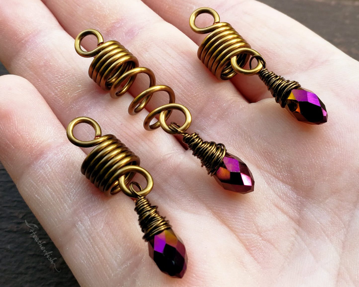 Set of 3 purple gold loc jewelry held in hand to show scale.