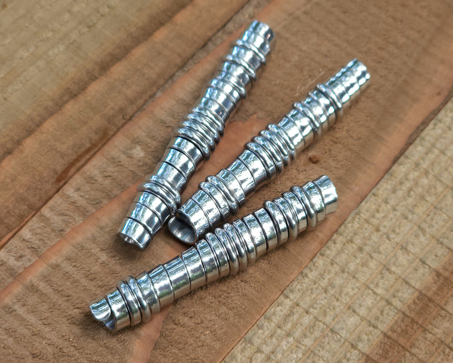 Three aluminum hair beads on a wood surface.