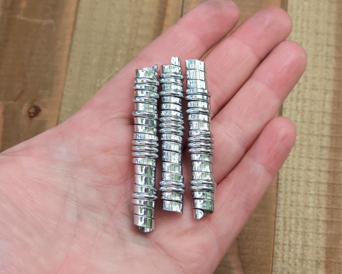 Three aluminum hair beads held in a hand to show scale.