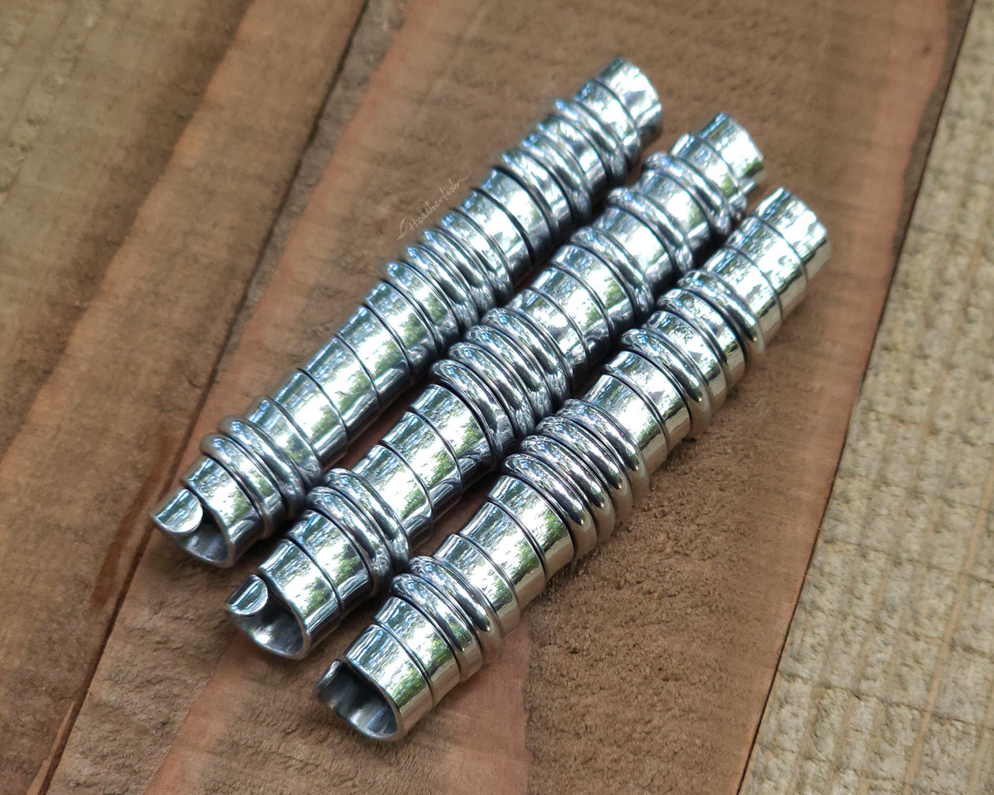 Three aluminum hair beads on a wood surface.