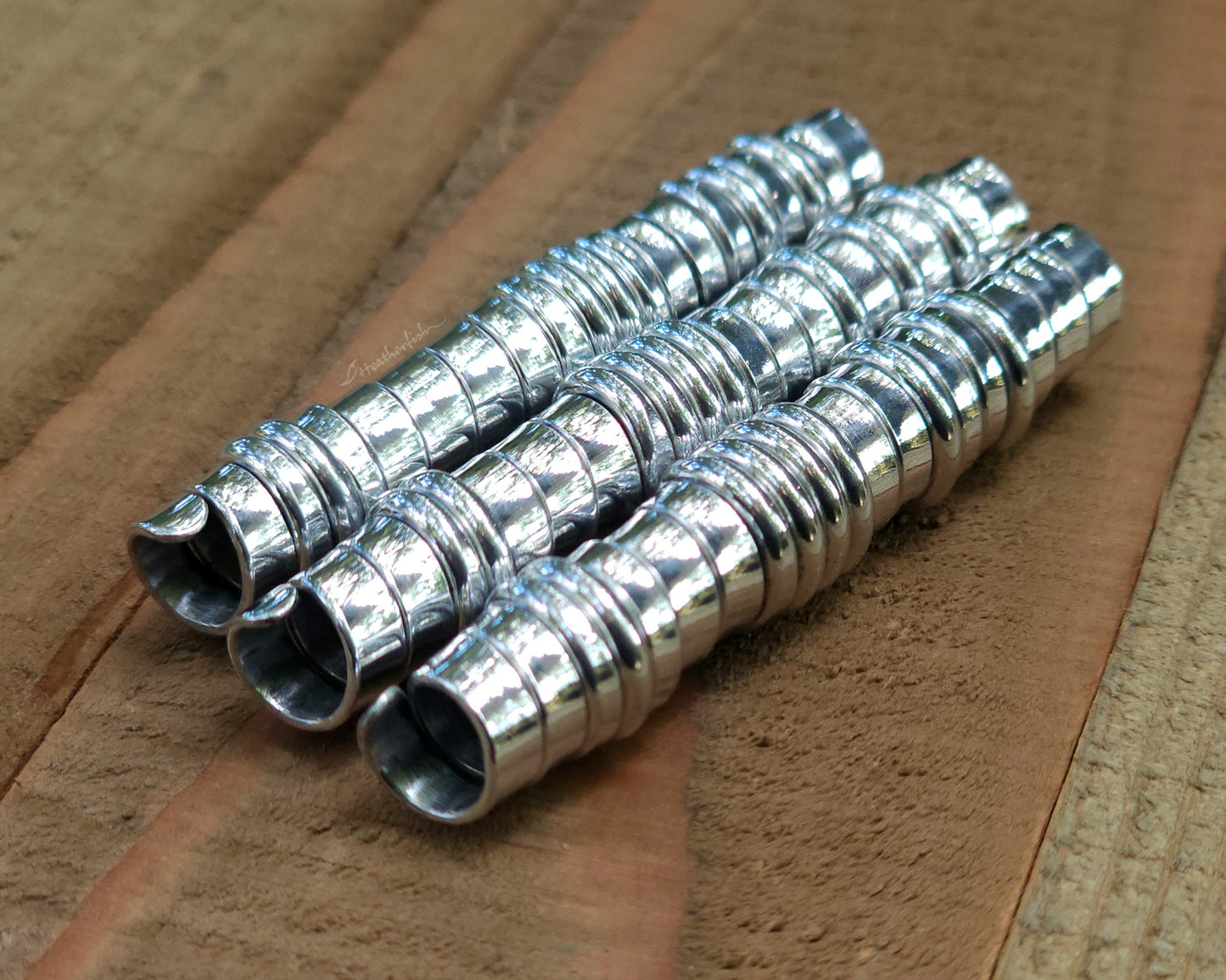 Three aluminum hair beads on a wood surface.