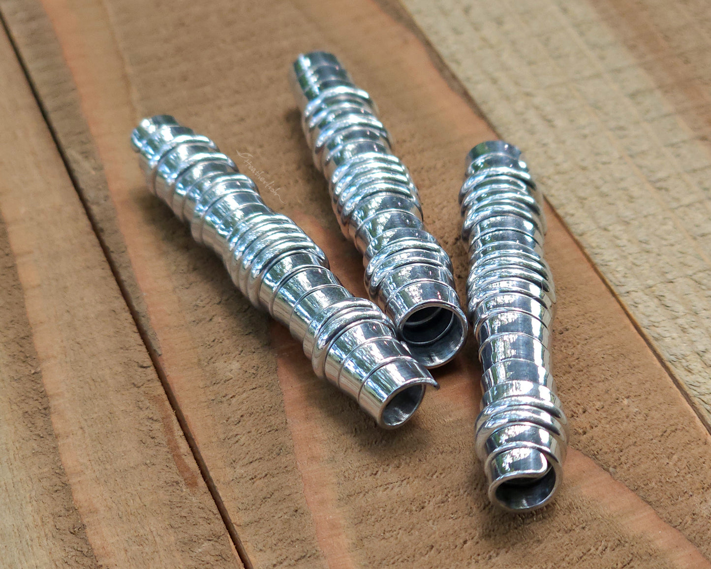 Three aluminum hair beads on a wood surface.