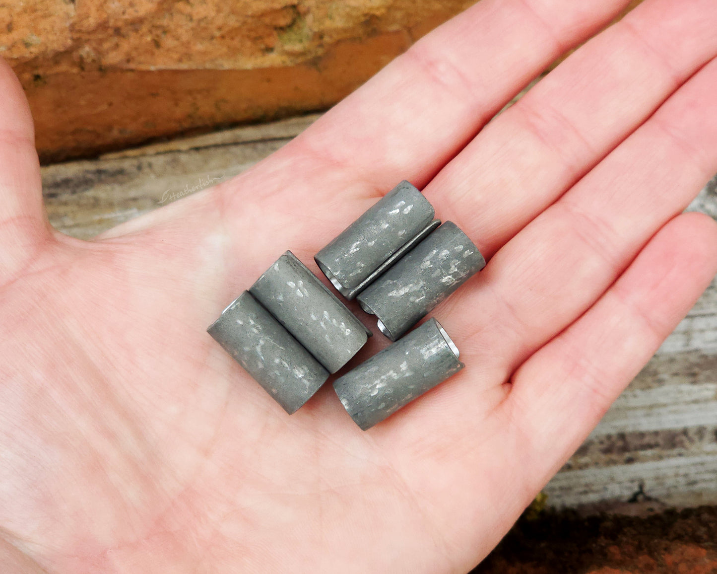 Set of 5 textured oxidized aluminum hair cuffs for locs, dreadlocks, braids, or beards, in a matte grey. Held in hand to show scale.