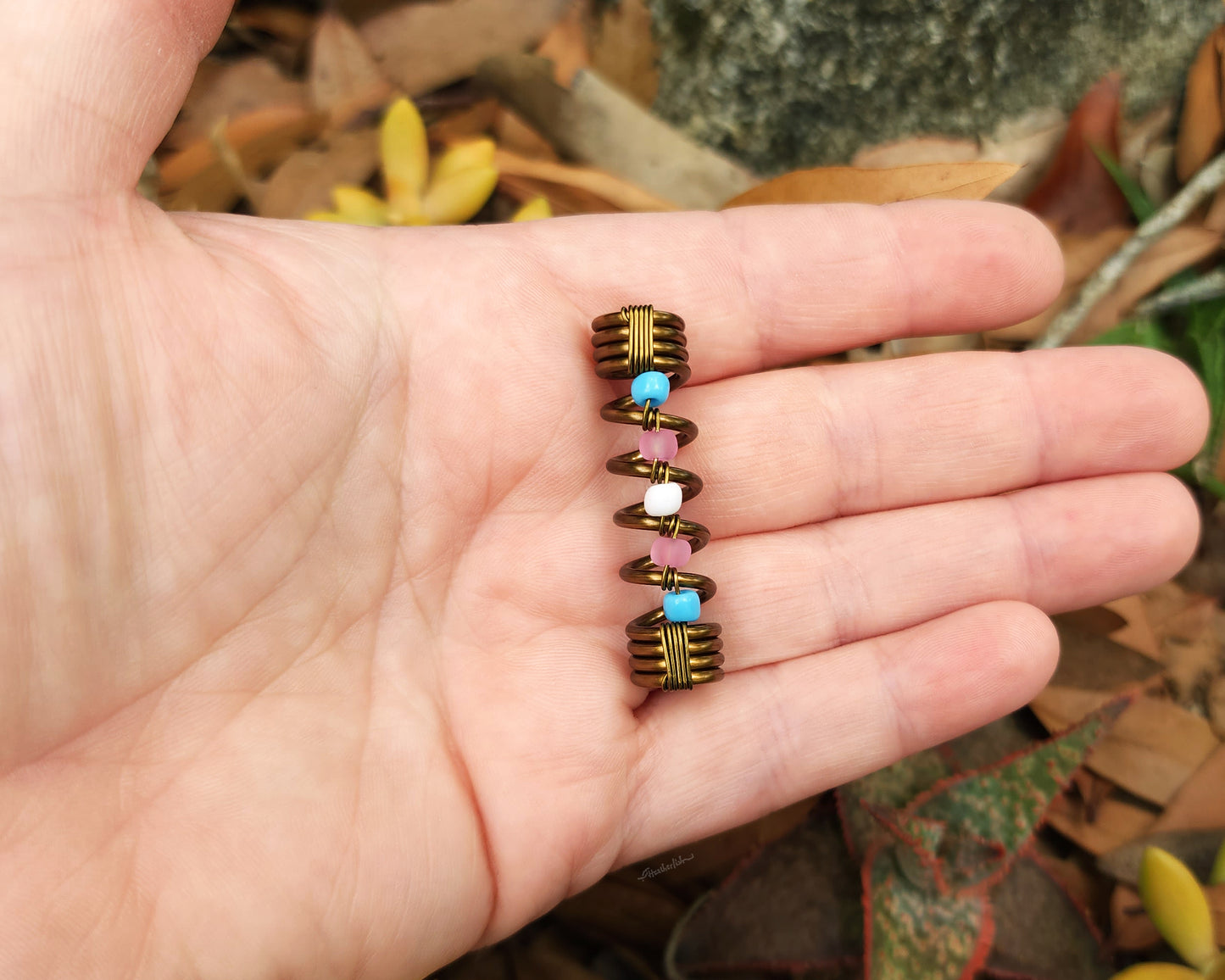 Trans pride loc bead held in hand to show scale.