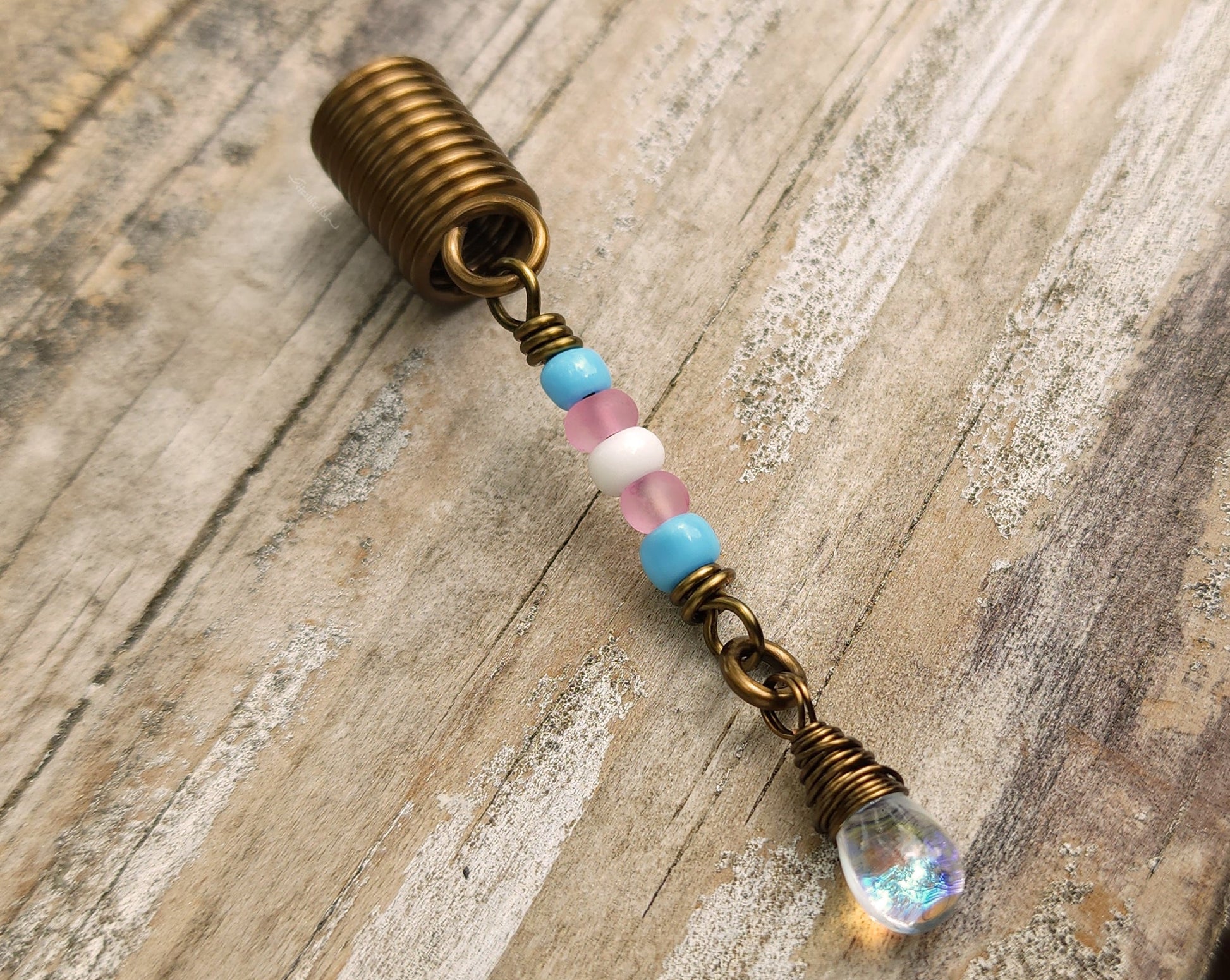 A trans pride hair bead on a wood background.