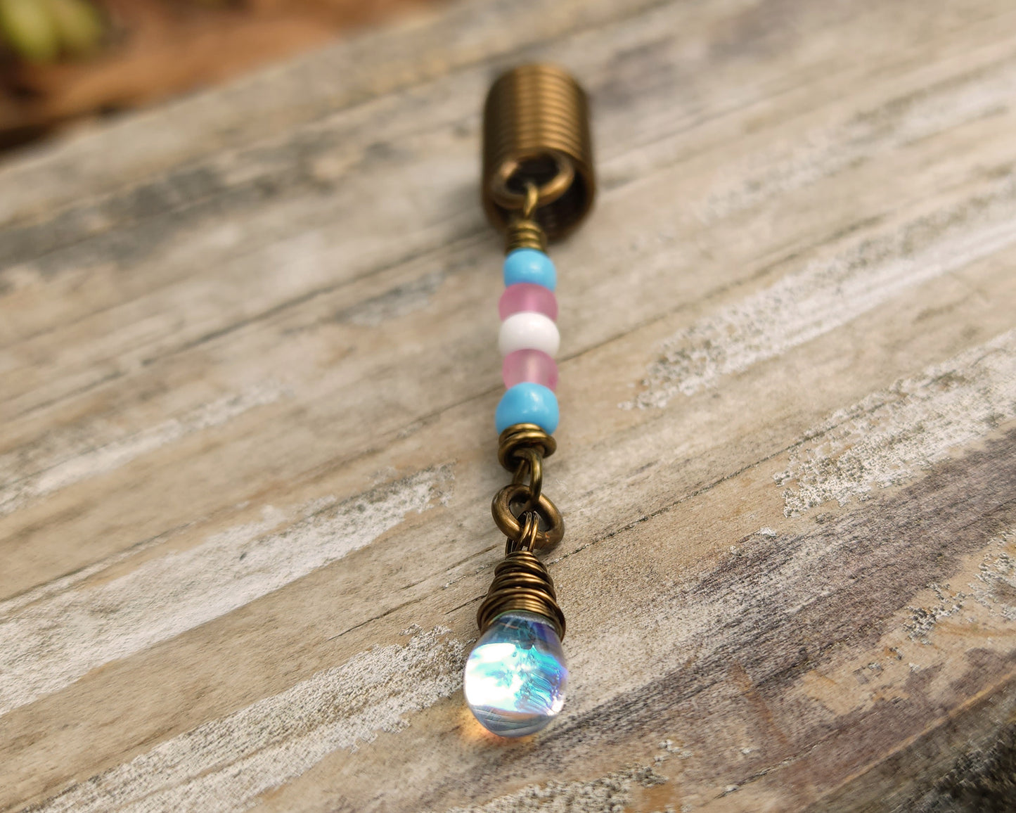 A trans pride hair bead on a wood background.
