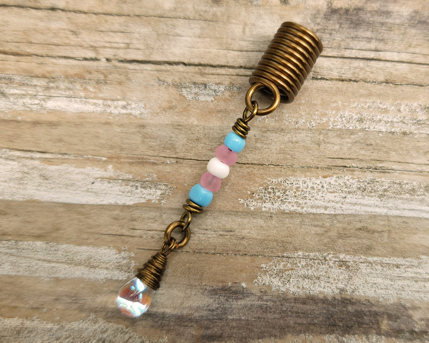 A trans pride hair bead on a wood background.