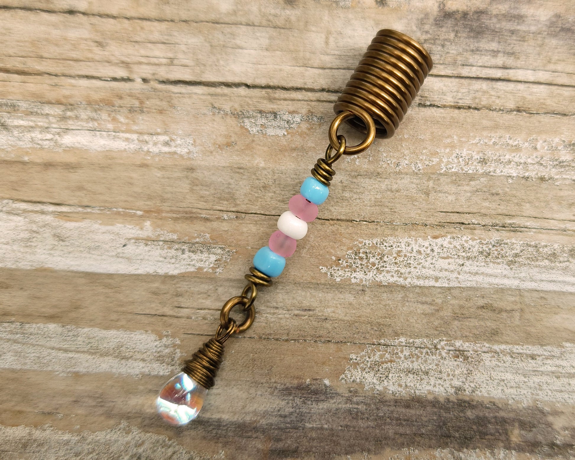 A trans pride hair bead on a wood background.