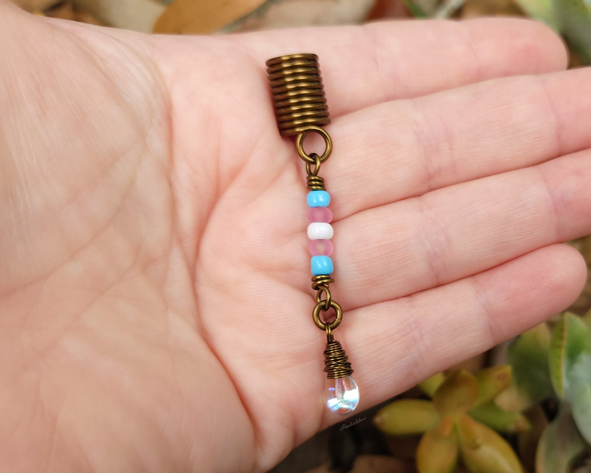 A trans pride hair bead held in hand to show scale.