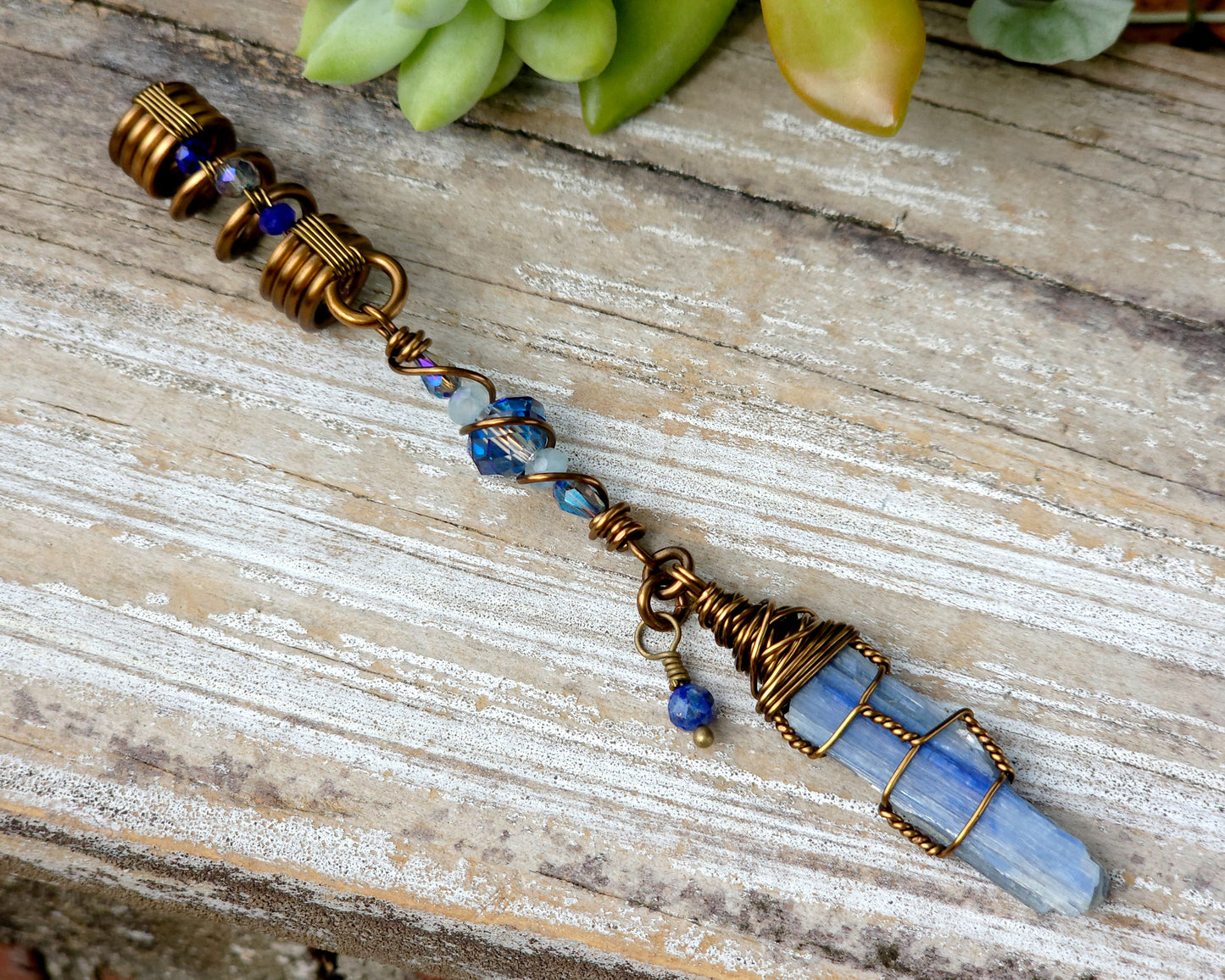 A blue kyanite hair bead with lapis lazuli and glass accents displayed on a wood background.