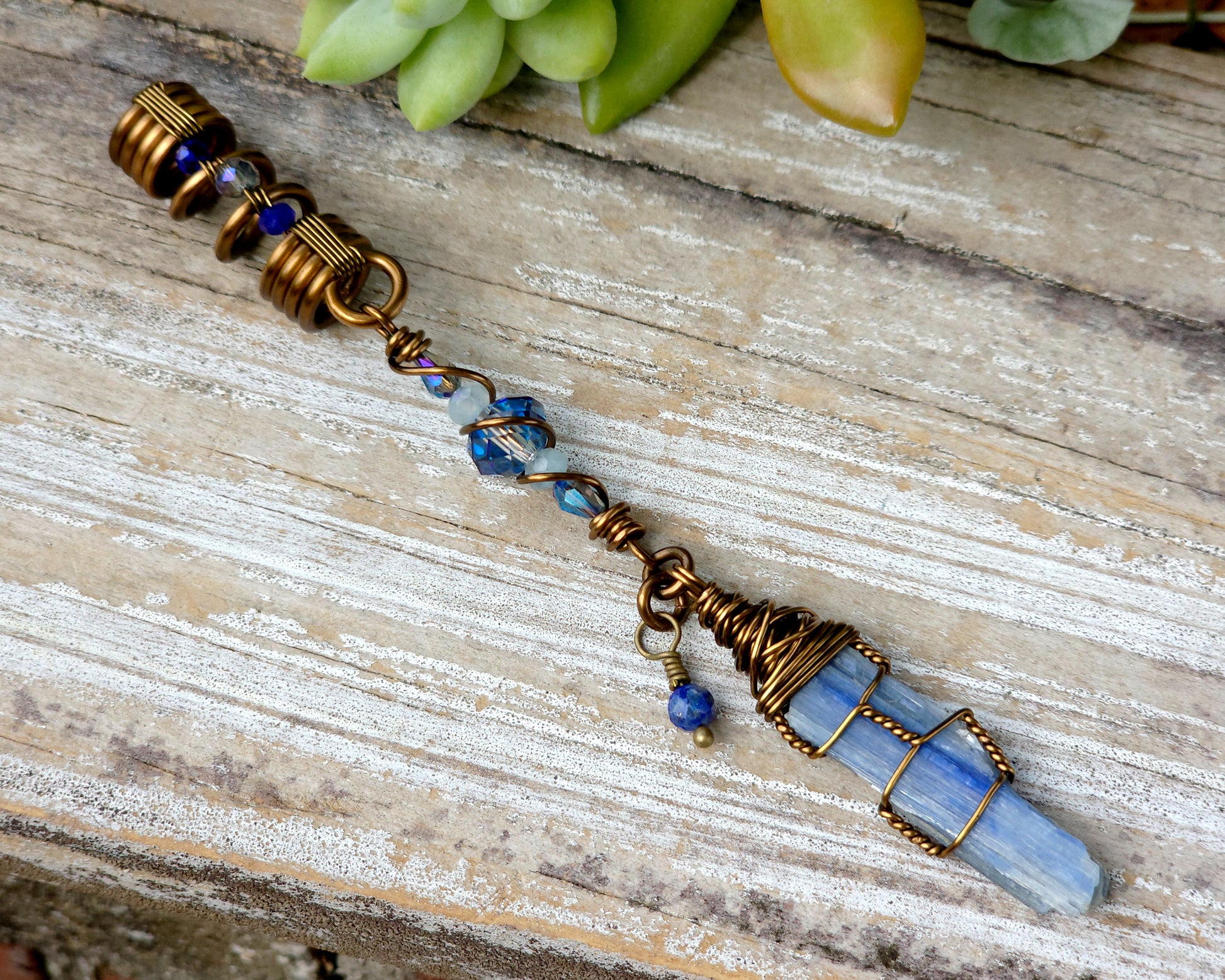 A blue kyanite hair bead with lapis lazuli and glass accents displayed on a wood background.