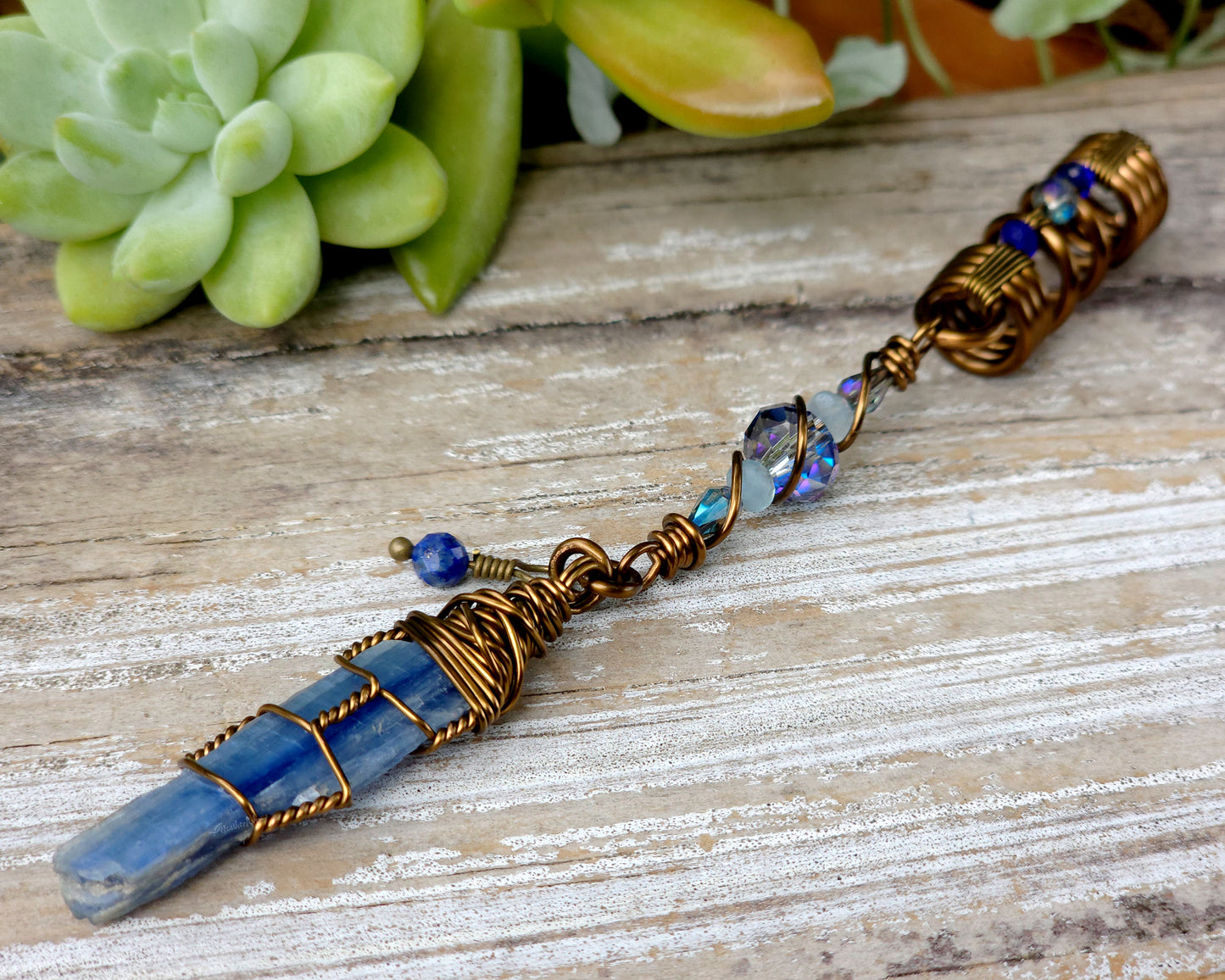 A blue kyanite hair bead with lapis lazuli and glass accents displayed on a wood background.