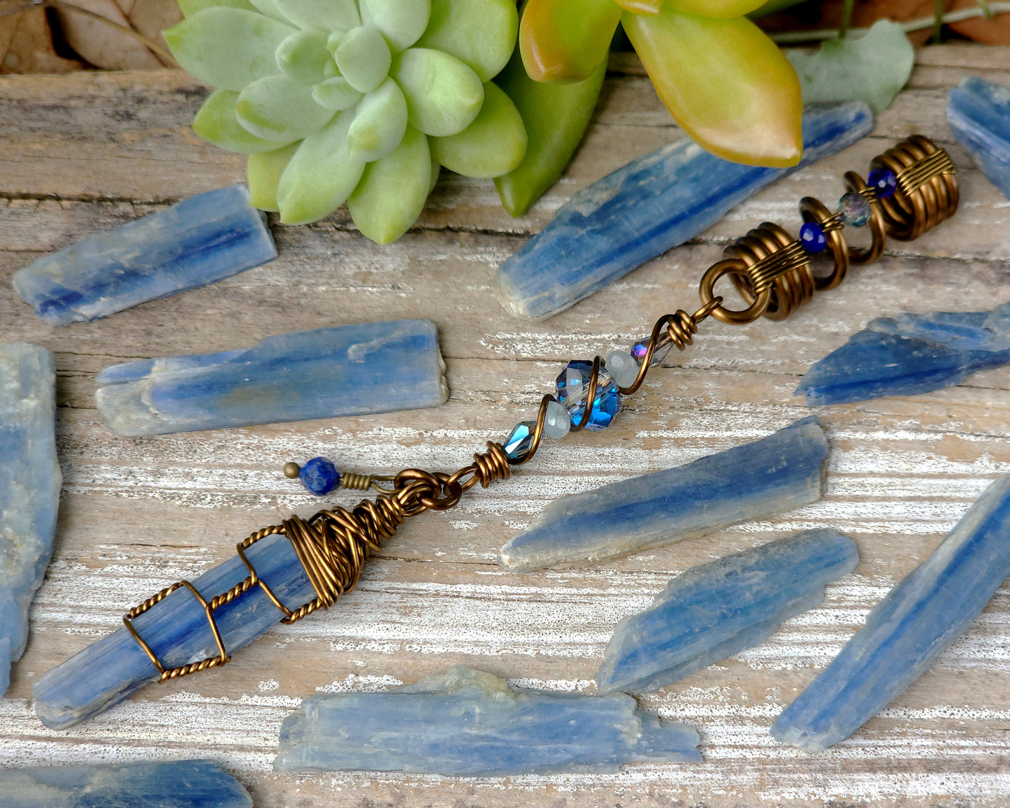 A blue kyanite hair bead with lapis lazuli and glass accents displayed on a wood background, and surrounded by loose blue kyanite crystals.