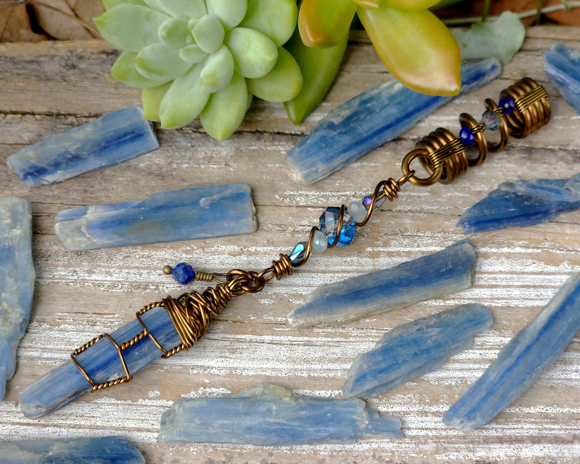 A blue kyanite hair bead with lapis lazuli and glass accents displayed on a wood background, and surrounded by loose blue kyanite crystals.