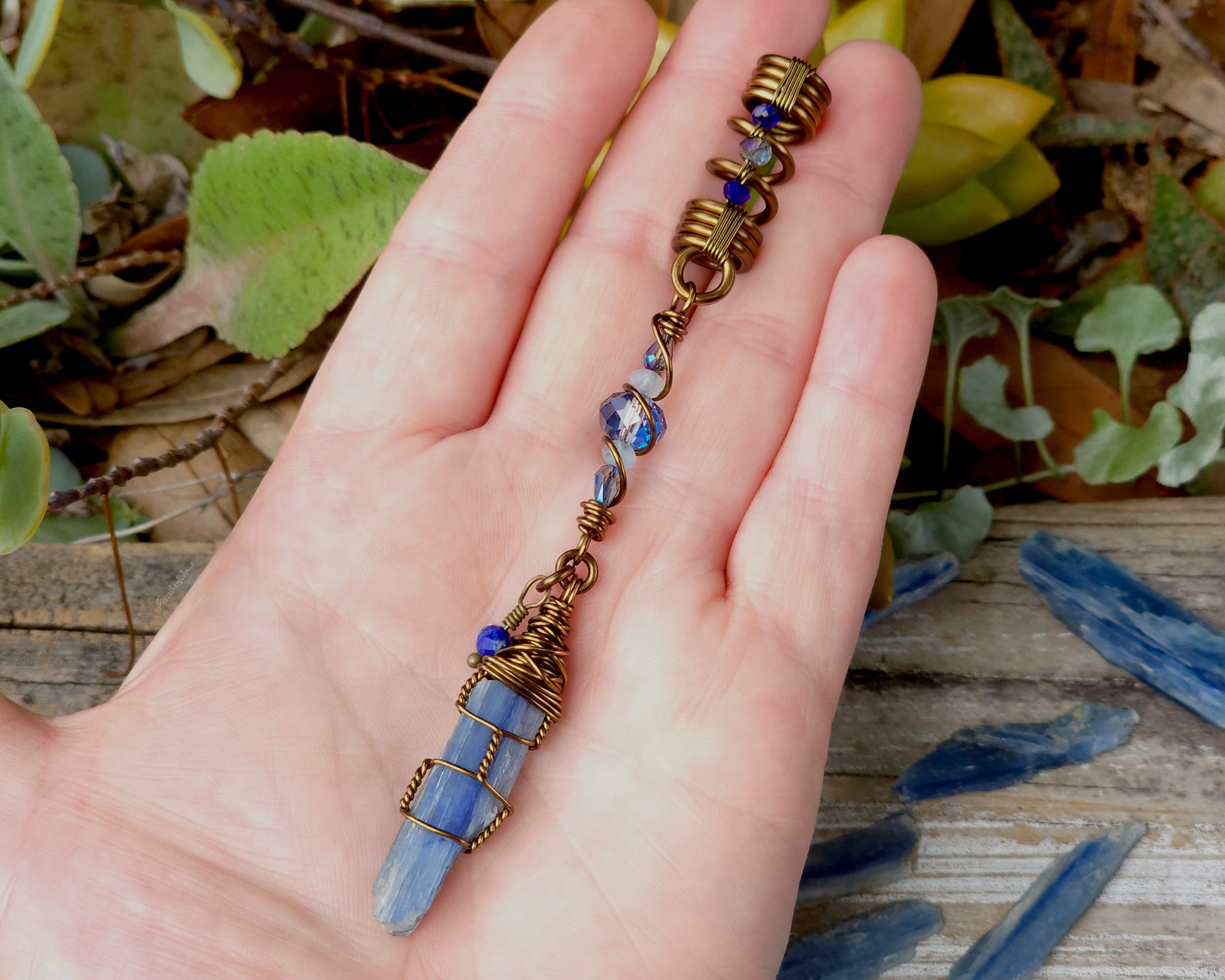 A blue kyanite hair bead with lapis lazuli and glass accents held in a hand to show scale.