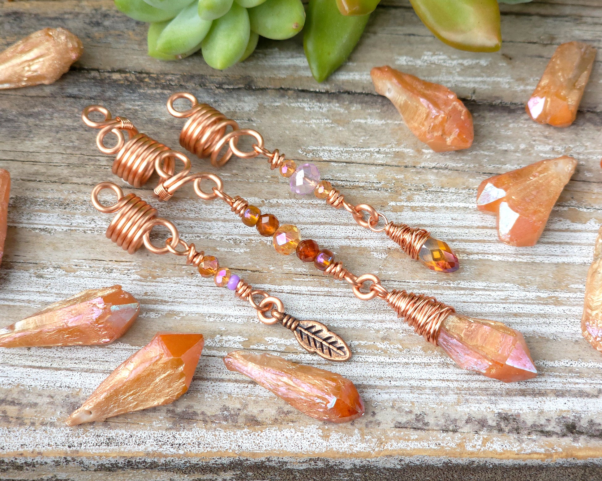 Set of three orange aura loc beads on a wood board surrounded by loose orange aura crystals.