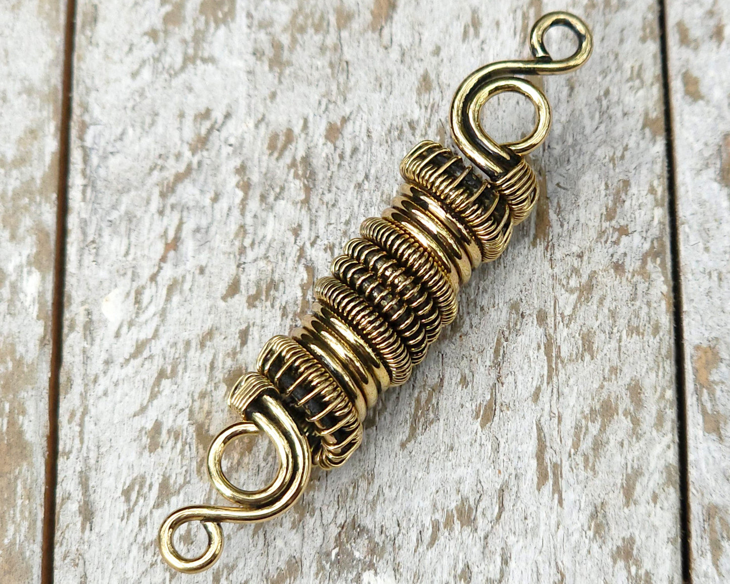 Woven brass dreadlock bead on a wood background.