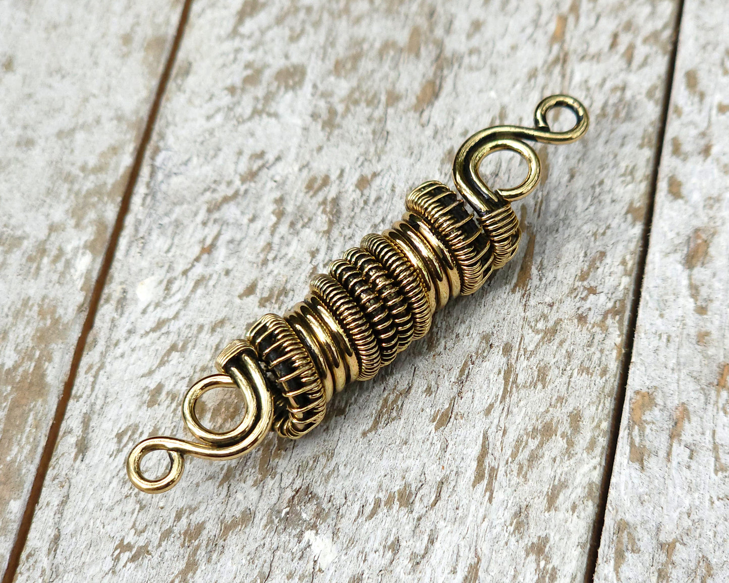 Woven brass dreadlock bead on a wood background.