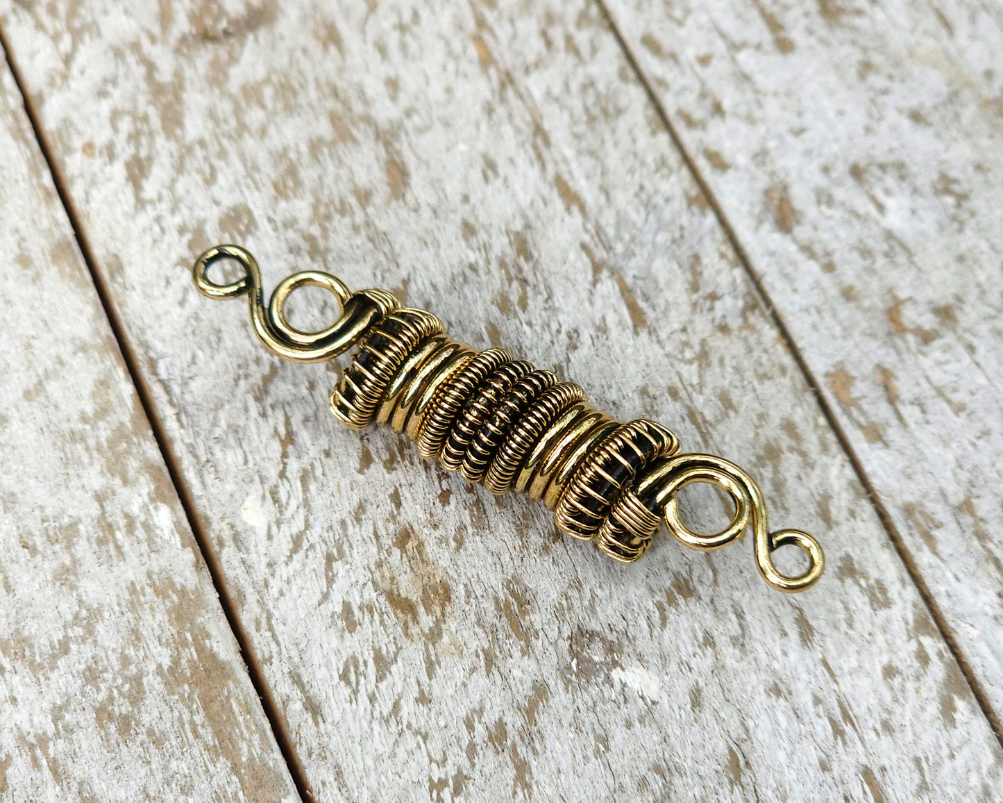 Woven brass dreadlock bead on a wood background.