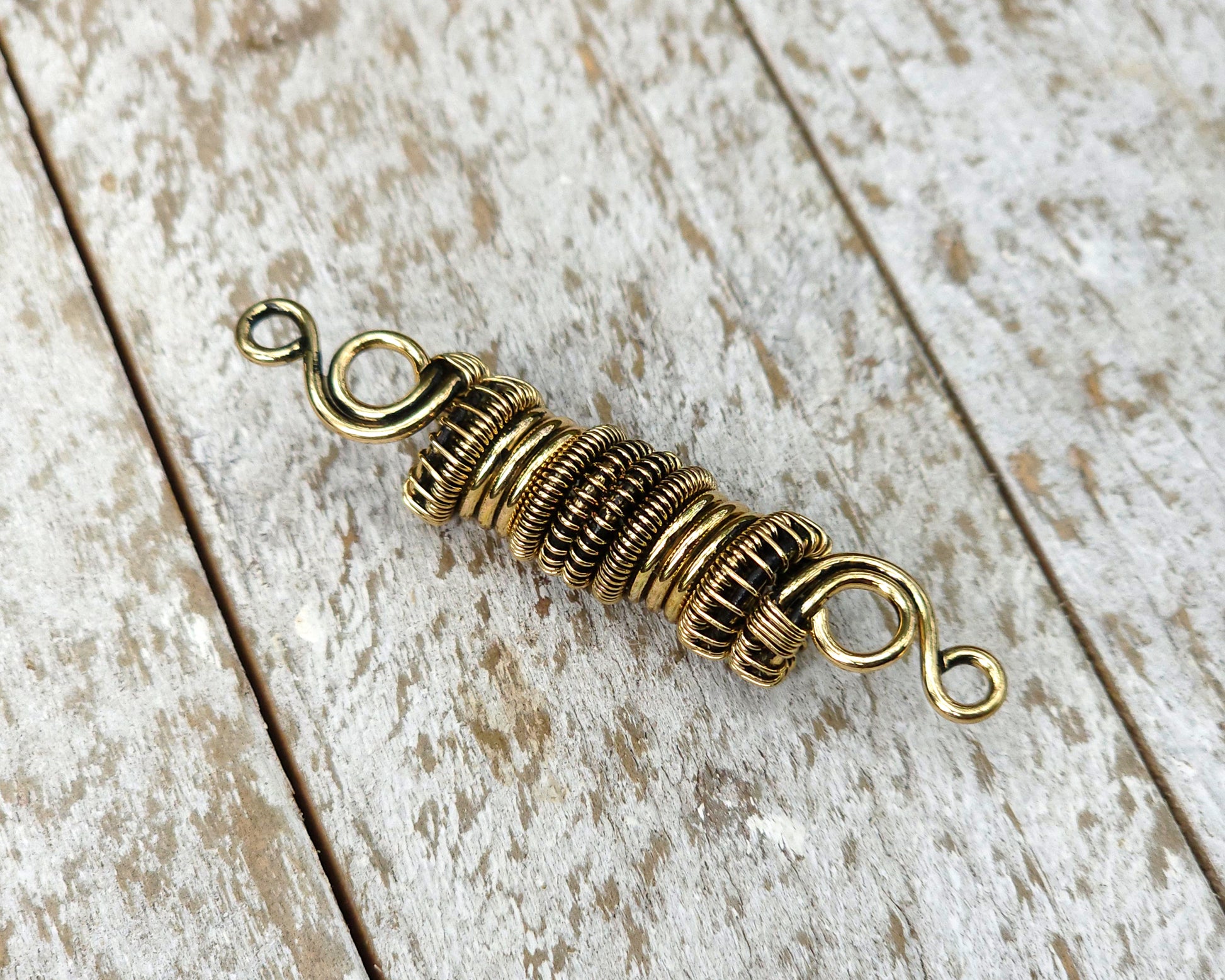 Woven brass dreadlock bead on a wood background.