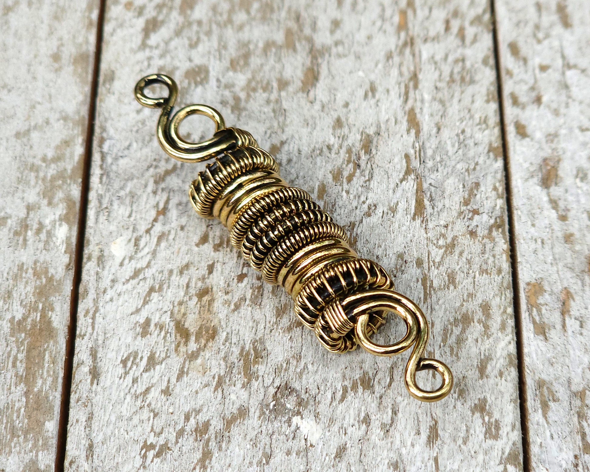 Woven brass dreadlock bead on a wood background.
