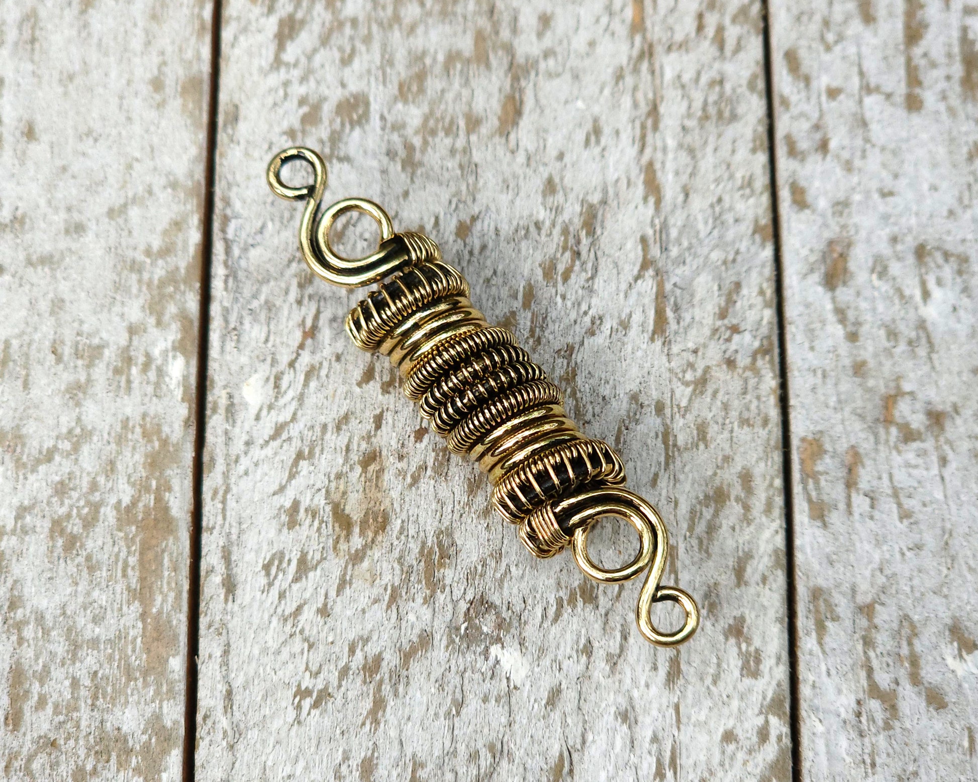 Woven brass dreadlock bead on a wood background.