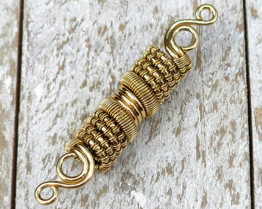 Woven brass dreadlock bead on a wood background.