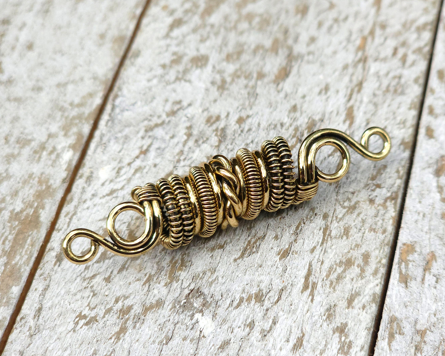 Woven brass dreadlock bead on a wood background.