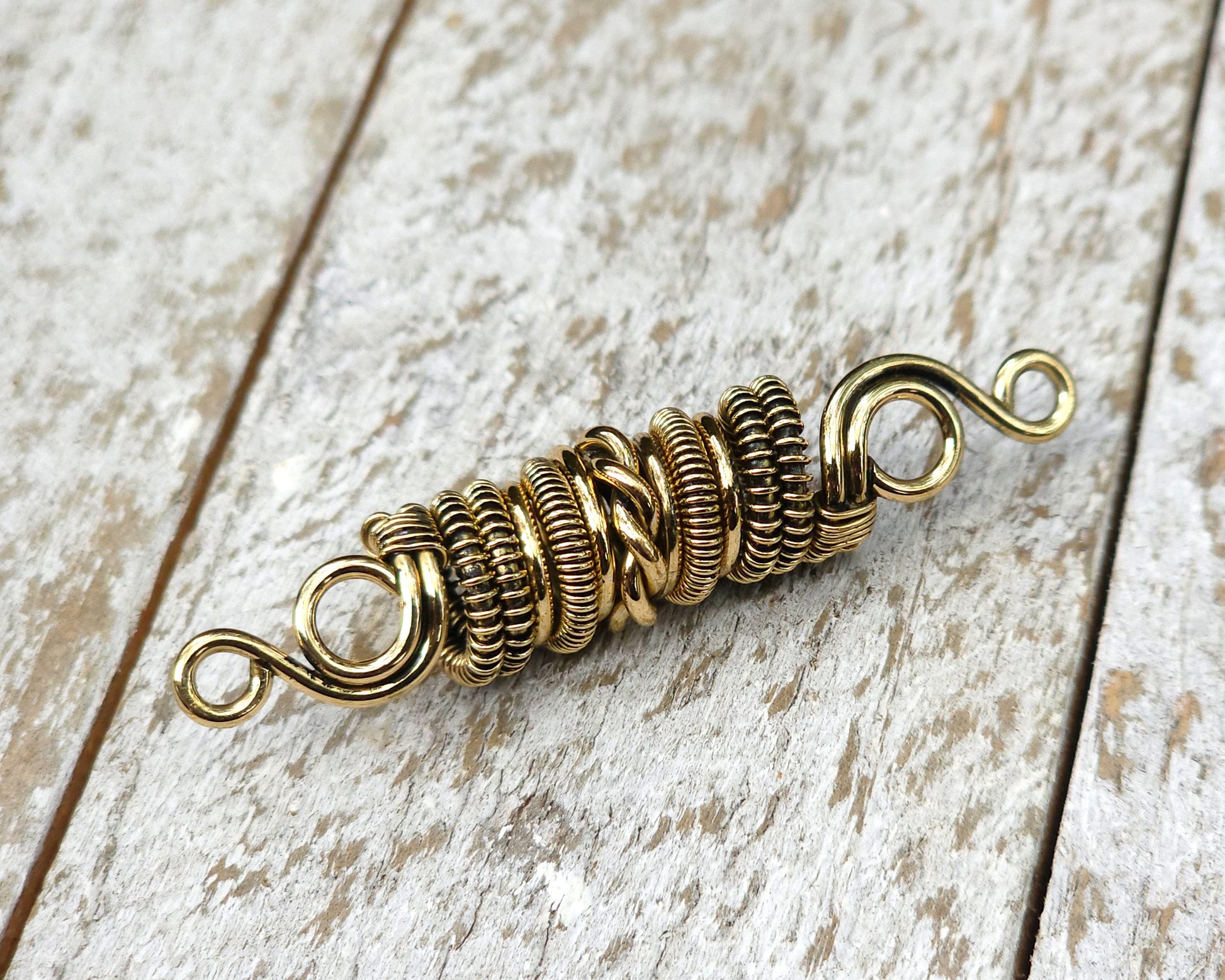 Woven brass dreadlock bead on a wood background.