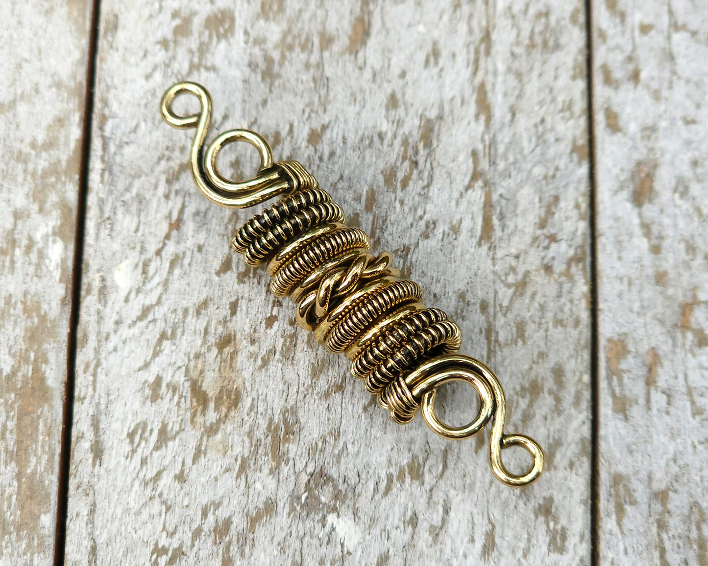 Woven brass dreadlock bead on a wood background.