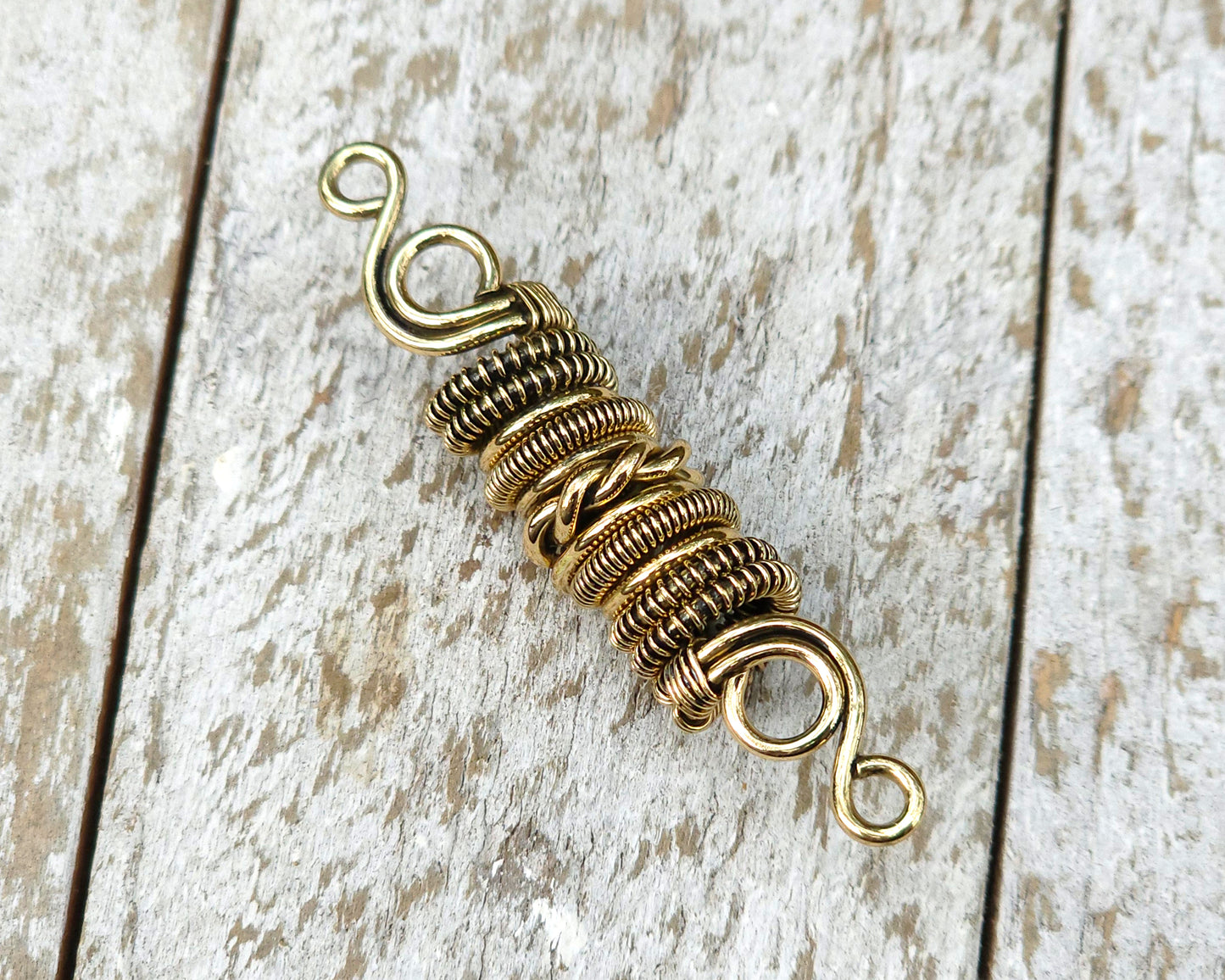 Woven brass dreadlock bead on a wood background.