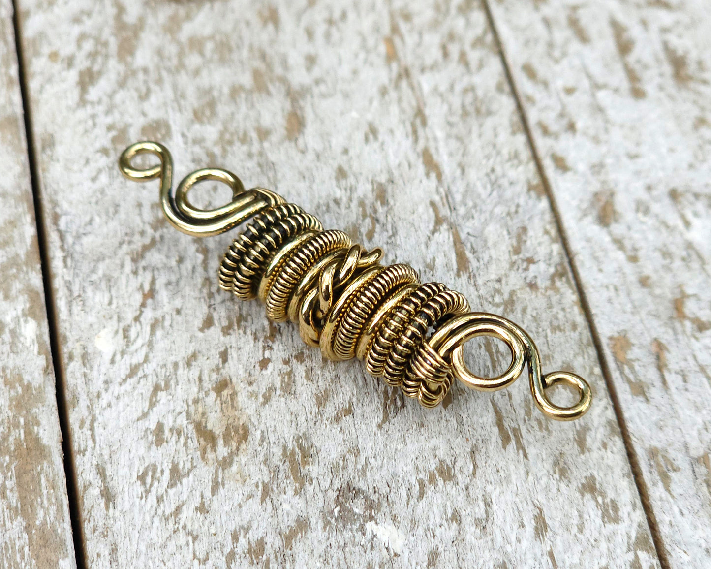 Woven brass dreadlock bead on a wood background.