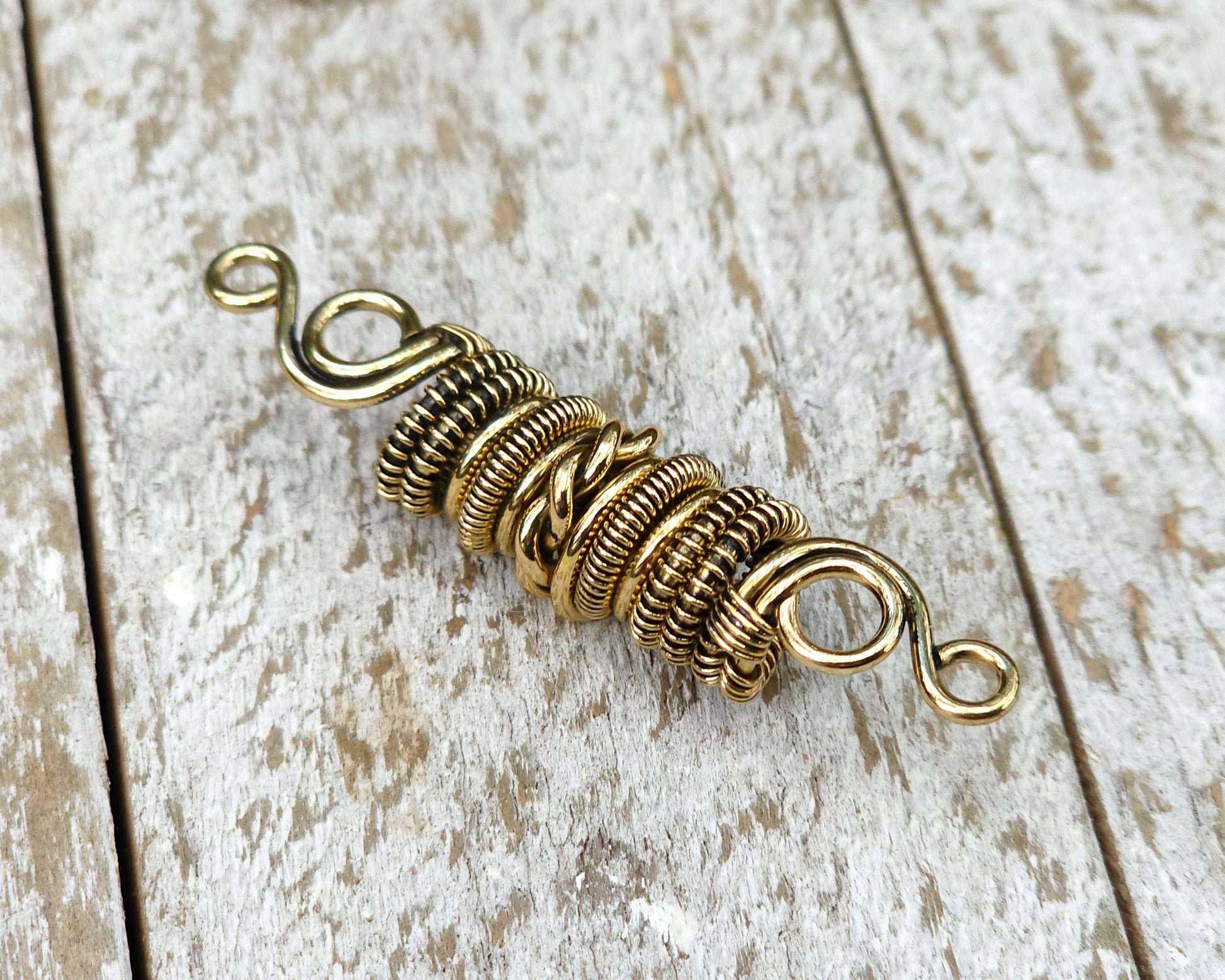Woven brass dreadlock bead on a wood background.