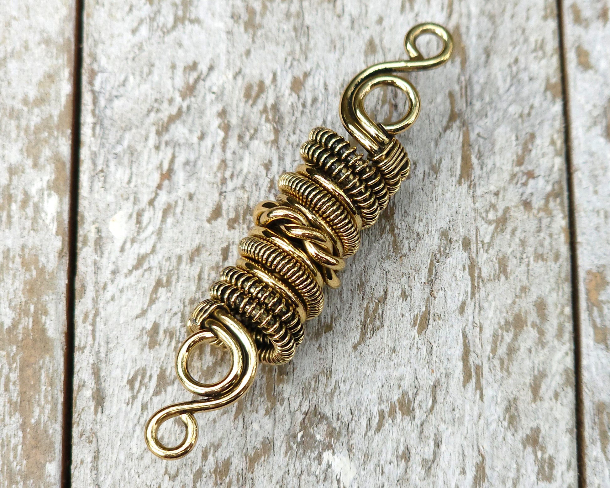 Woven brass dreadlock bead on a wood background.