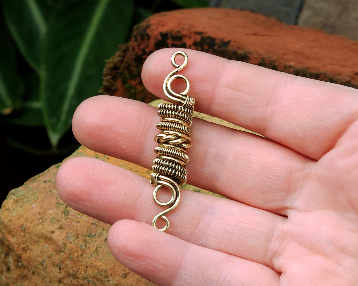 Woven brass dreadlock bead held in hand to show scale.
