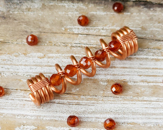 Orange garnet dreadlock bead on a board surrounded by loose garnet stones.