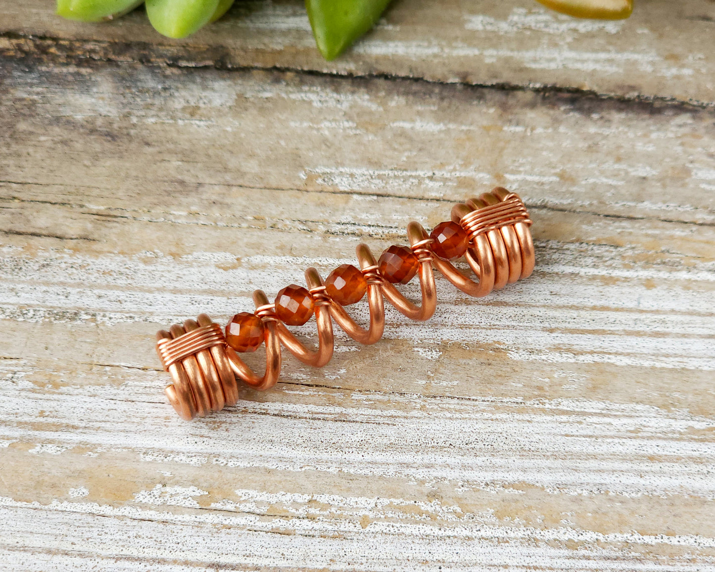 Orange garnet dreadlock bead on a wood board.