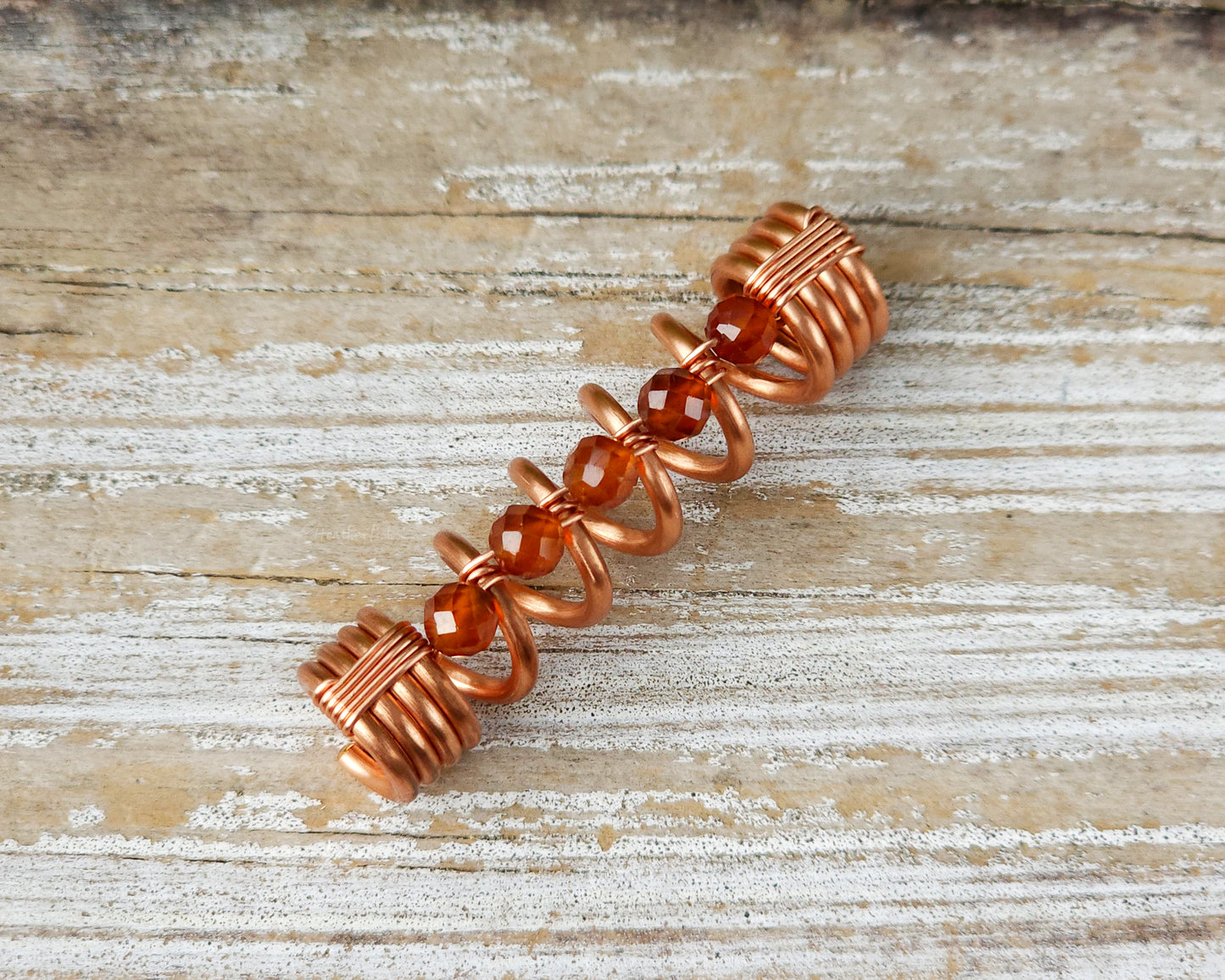 Orange garnet dreadlock bead on a wood board.