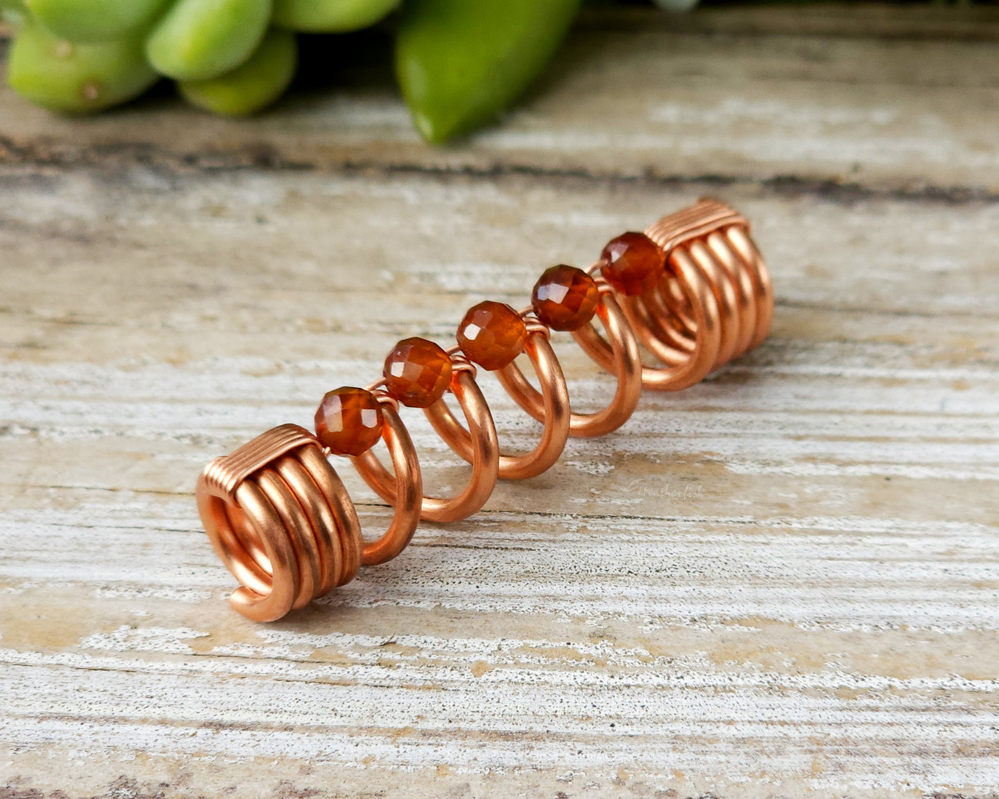Orange garnet dreadlock bead on a wood board.