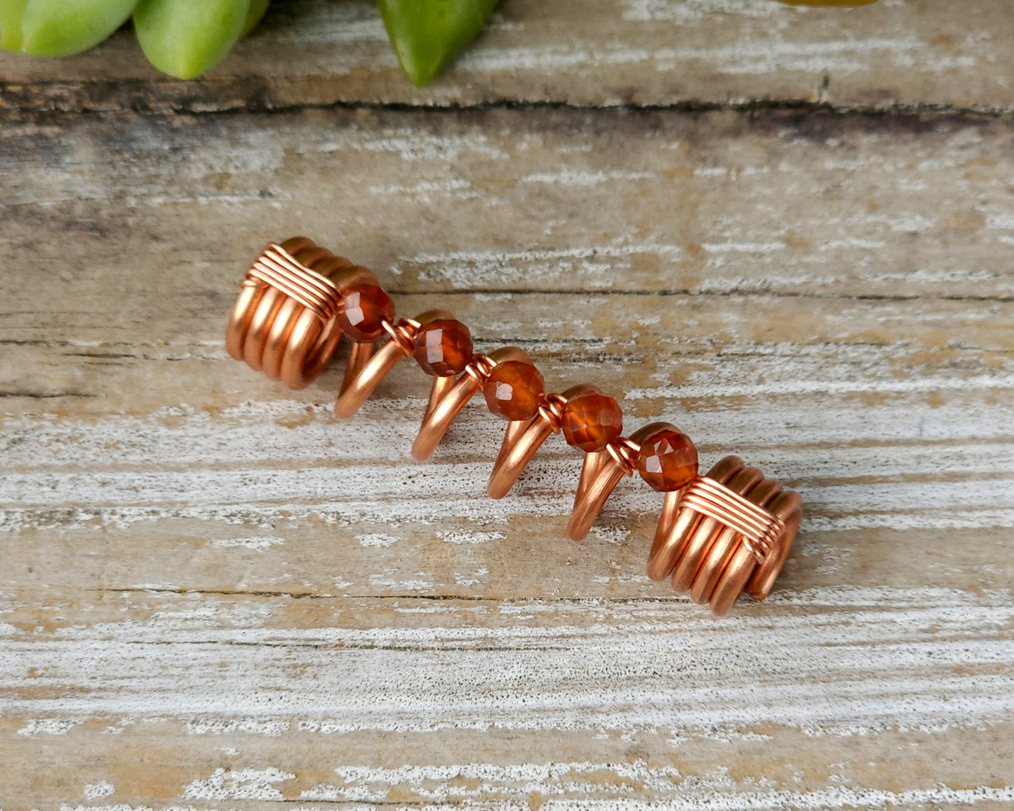 Orange garnet dreadlock bead on a wood board.