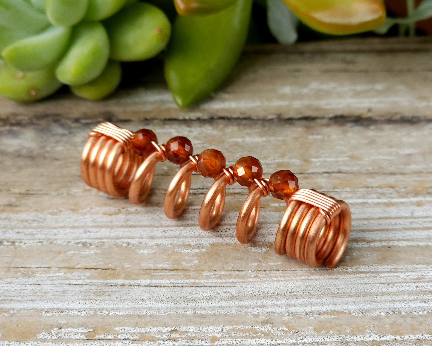 Orange garnet dreadlock bead on a wood board.