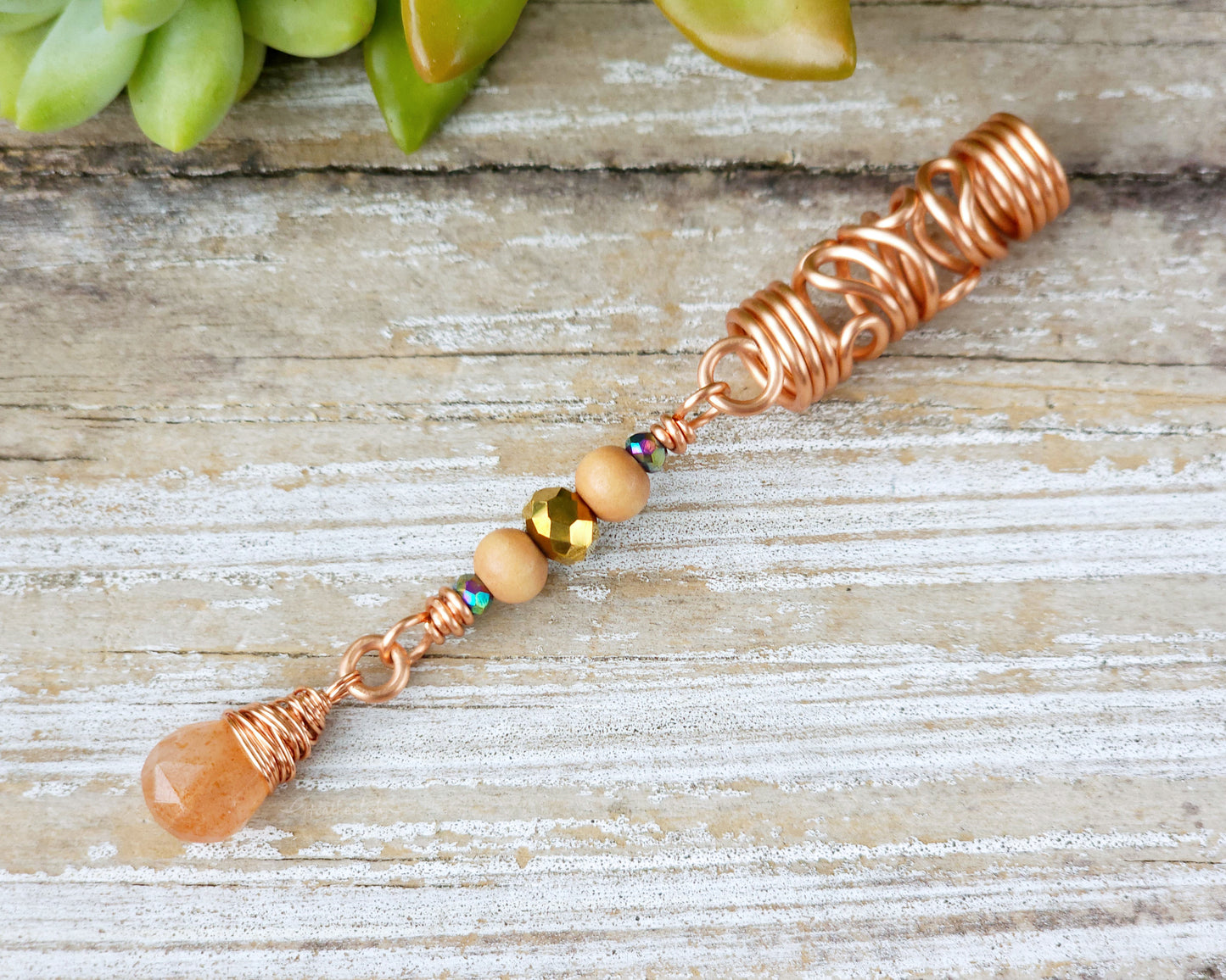 Sunstone squiggle dreadlock bead on a wood board.