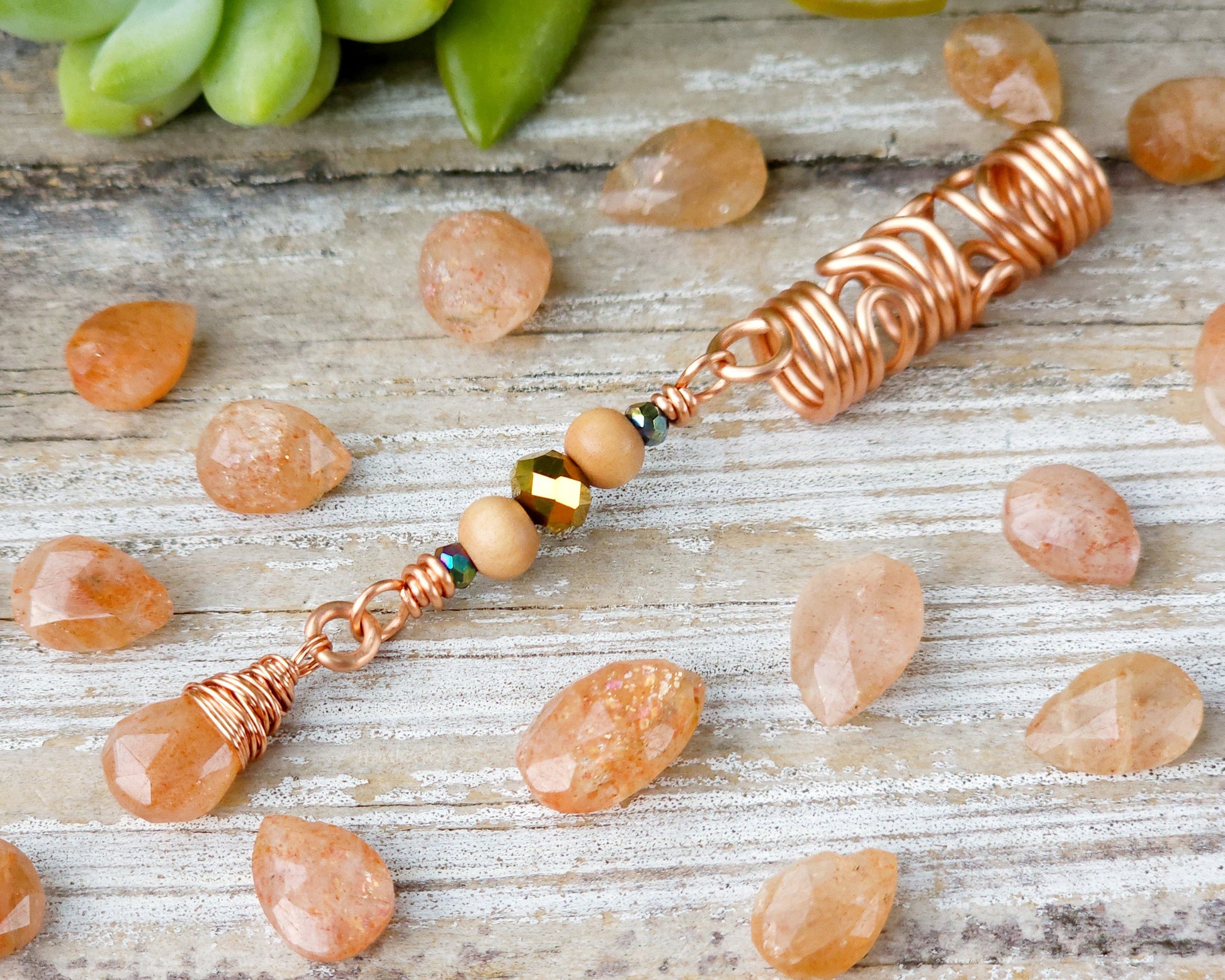Sunstone squiggle dreadlock bead on a wood board surrounded by scattered sunstones.