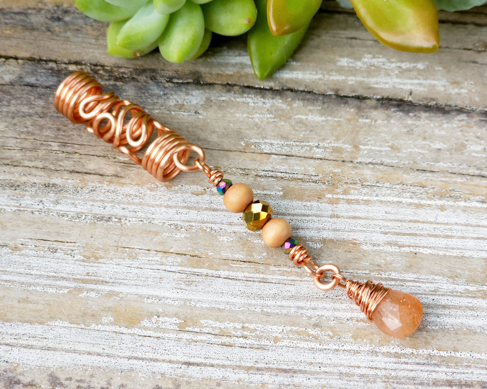 Sunstone squiggle dreadlock bead on a wood board.