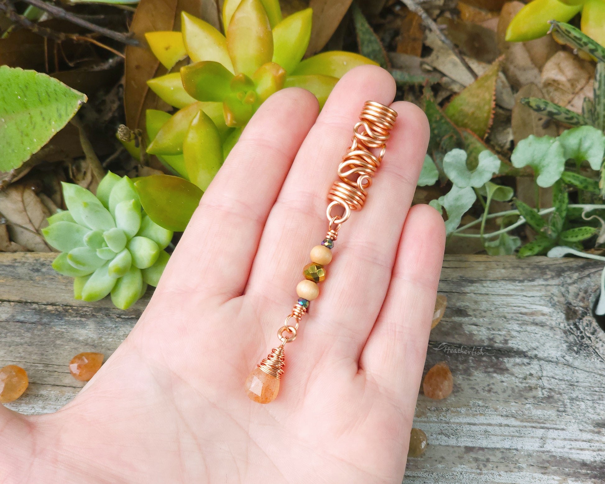 Sunstone squiggle dreadlock bead held in a hand over a wood board.