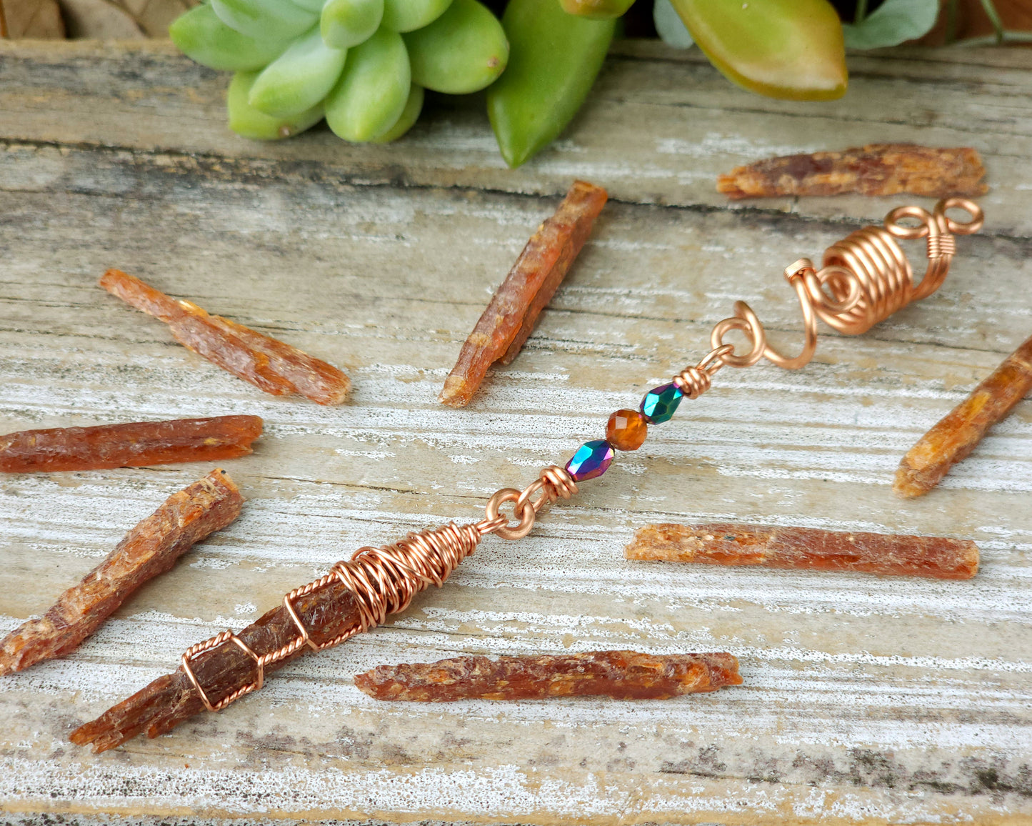 Mini orange kyanite hair bead on a wood board surrounded with loose orange kyanite shards.