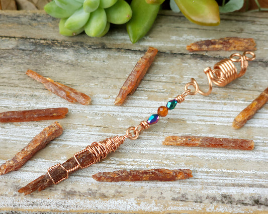 Mini orange kyanite hair bead on a wood board surrounded with loose orange kyanite shards.
