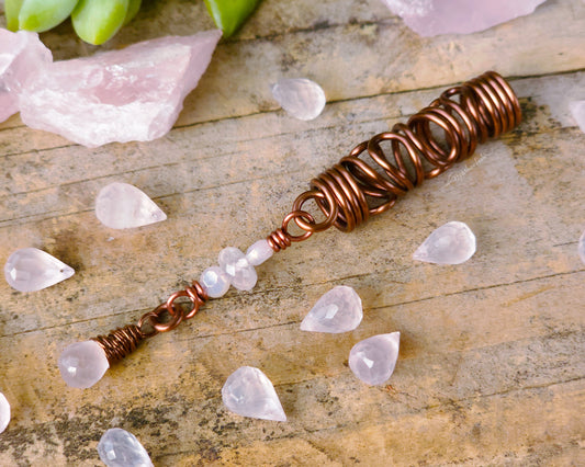 Rose quartz squiggle dreadlock bead on a wood board surrounded by loose rose quartz beads.