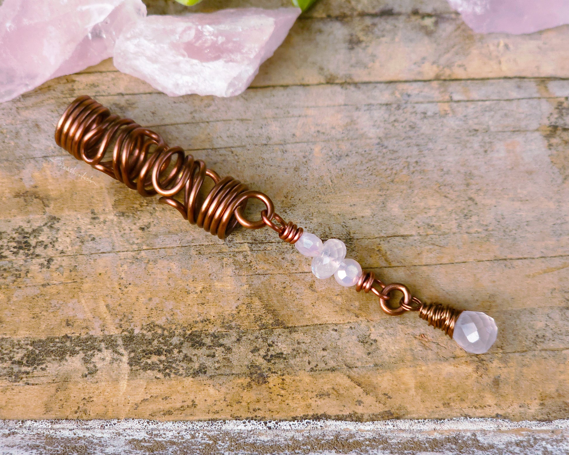 Rose quartz squiggle dreadlock bead on a wood board.
