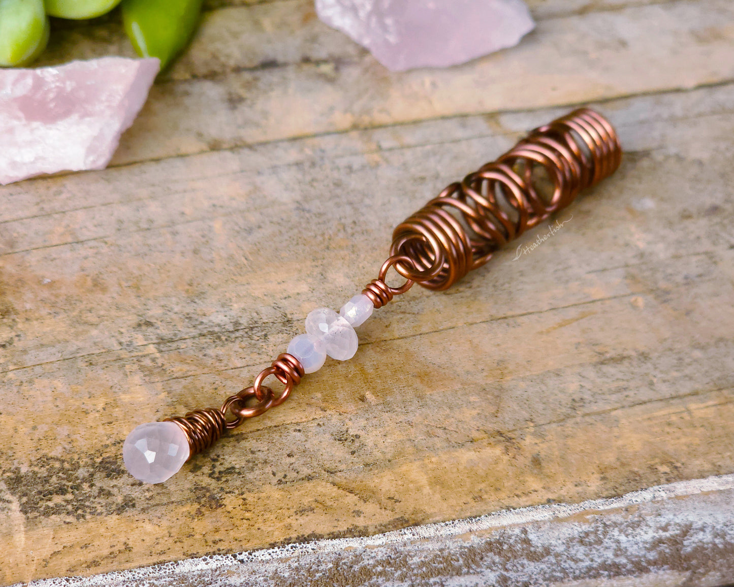 Rose quartz squiggle dreadlock bead on a wood board.